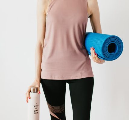 Faceless slim female athlete in sportswear standing with blue fitness mat and water bottle while preparing for indoors workout
